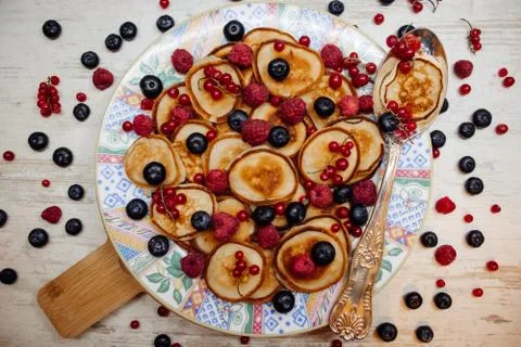 Mini pancakes with berries on a patterned plate with silver spoon in rustic s Stock Photos