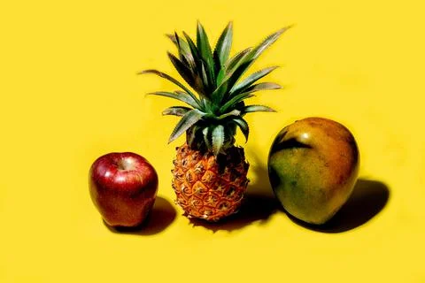 Mini pineapple, mango and apple on a solid yellow background Foto stock