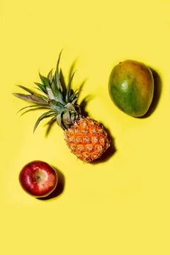 Mini pineapple, mango and apple on a solid yellow background Stock Photos