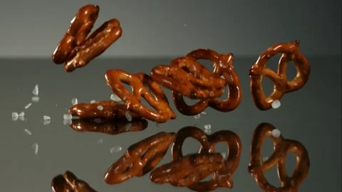 Mini pretzels falling and scattering on dark reflective surface Stock Footage 327513898