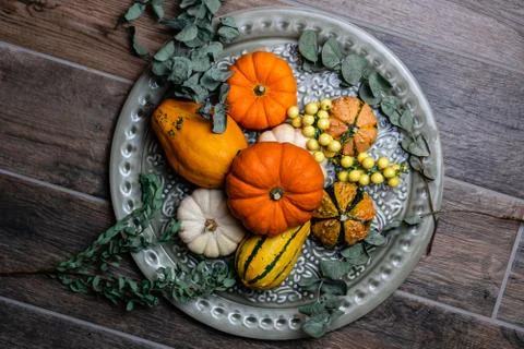 Mini pumpkin composition on a plate with greenery and rustic floor tiles Stock Photos