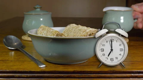 Mini ringing alarm clock, dry wheat cereal bowl and hand putting down hot milk. Video stock 170424809