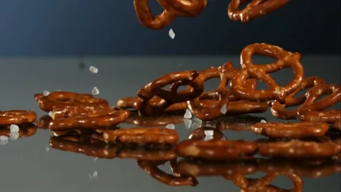 Mini salted pretzels fall and bounce on a dark mirror surface in slow motion Stock Footage 326628011