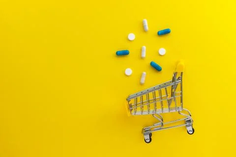 Mini shopping cart, pills and capsules on yellow background. Online drugstore Stock Photos
