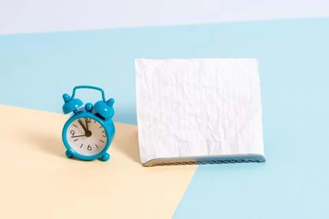 Mini small size alarm clock beside a Paper sheet placed tilted. Notepaper on the Stock Photos