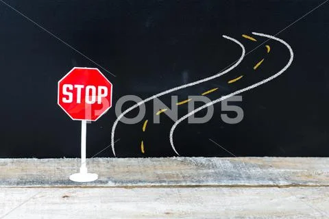 Mini STOP sign in front of curved road, hand drawing over chalkboard Stock Photos