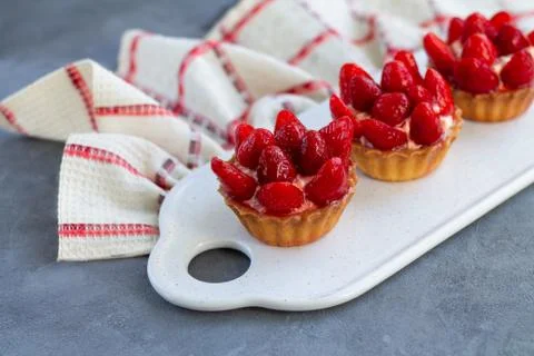 Mini strawberry tartlets on ceramic board with linen napkin on stone table Stock Photos
