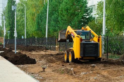 Mini tractor with a bucket at work on a construction site. Small Yellow Backh Stock Photos