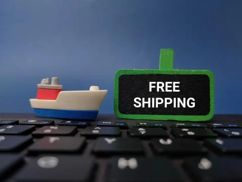 A miniature cargo ship sits on a computer keyboard next to a chalkboard sig.. Stock Photos