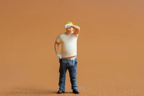 Miniature construction worker. He stands with one hand on his hip while wip.. Stock Photos