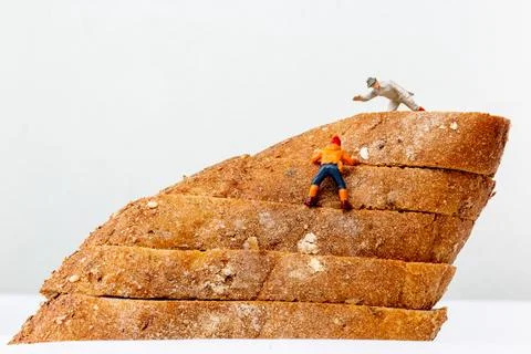 Miniature figurines climbing a stack of multigrain bread slices, resembling.. Stock Photos