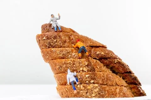 Miniature figurines climbing a stack of multigrain bread slices, resembling.. Foto stock