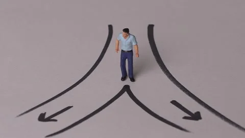 A miniature man standing in front of two crossroads. Concept about decision ma Stock Footage 232595576