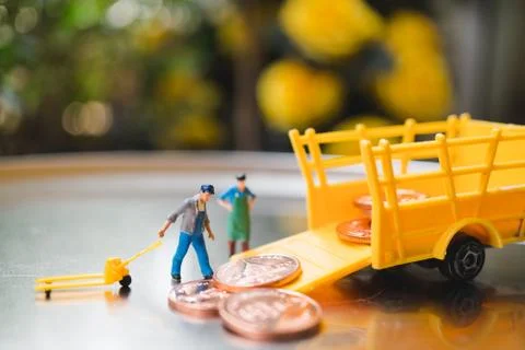 Miniature people, worker lifting stack coins into truck Foto stock