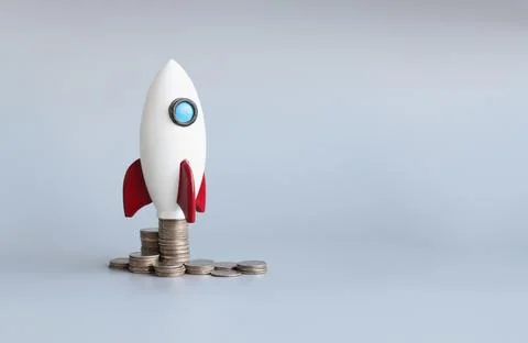 Miniature rocket stand on stack of coins, rocketship as symbol to open business Stockfoto's