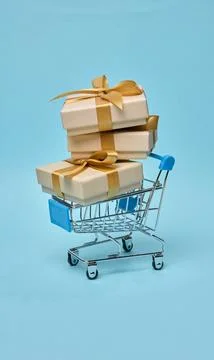 Miniature shopping cart with stack of gift boxes, beige packaging Stock Photos