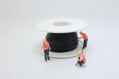 Miniature technicians working around large spool of cable Stock Photos