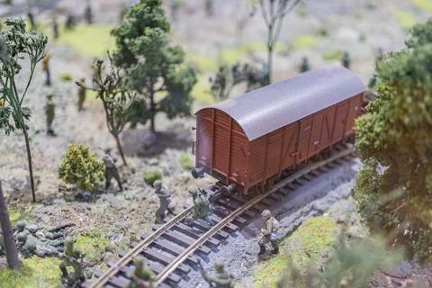 A miniature war scene features a model train set in a forested environment,.. Stock Photos