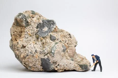 Miniature worker using a pickaxe to chip away at a large rock Stock Photos