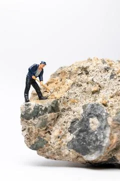 Miniature worker using a pickaxe to chip away at a large rock Foto stock