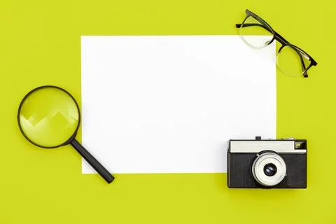 Minimal background with blank paper, camera and magnifier, flat lay. Stock Photos