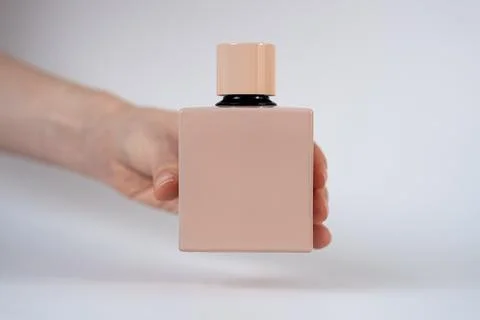 Minimal beige perfume bottle held by hand on neutral background Stock Photos