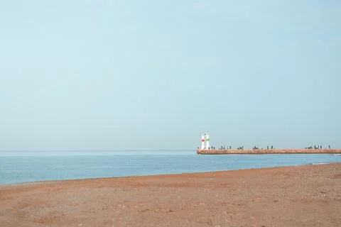 Minimal coastal landscape with distant lighthouse, calm sea, beach and clea.. Stock Photos