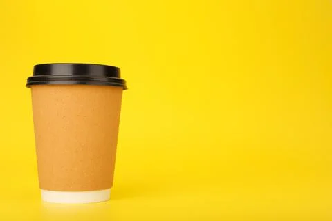 Minimal composition with brown cardboard cup of coffee on yellow background with Stock Photos