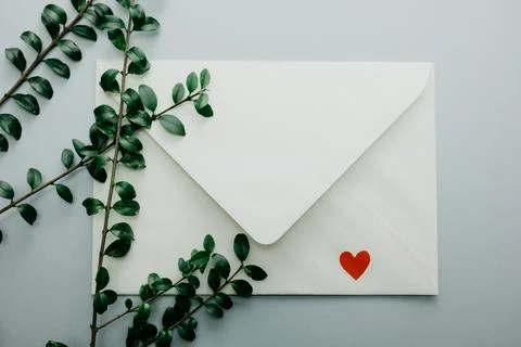 Minimal composition with a white envelope, heart and green leaves Stock Photos