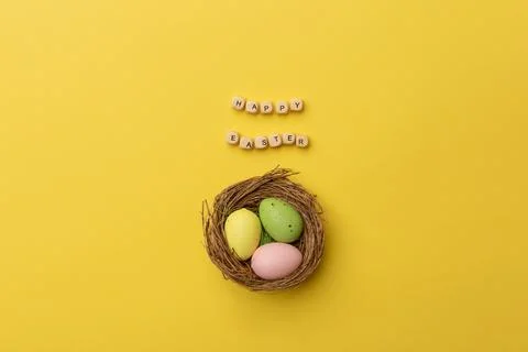 Minimal Easter concept. Nest with three colorful easter eggs with text Happy Stock Photos