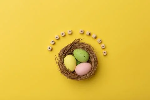 Minimal Easter concept. Nest with three colorful easter eggs with text Happy Stock Photos