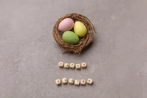 Minimal Easter concept. Nest with three colorful easter eggs with text Happy Stock Photos