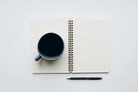Minimal flat lay of an open grid notebook, coffee and pen on white background Stock Photos