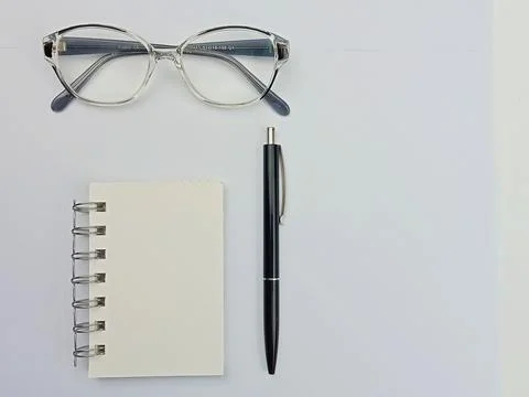 Minimal flat lay workspace with notebook, pen and glasses on white background Stock Photos
