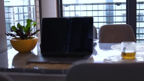 Minimal home office setup with a laptop on a dining table near a window, warm Stock Footage 320620967