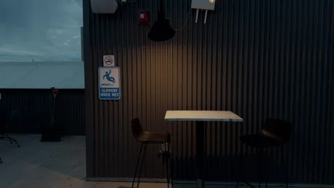 Minimal outdoor bar table and stools against corrugated metal wall at dusk Stock Footage 331644960