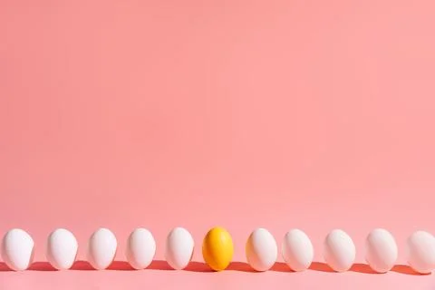 Minimal row of white eggs with one yellow egg on pink background Foto stock