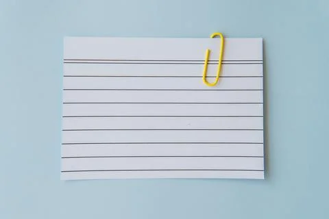 Minimal school paper concept with lined sheet and yellow paperclip on blue .. Stock Photos
