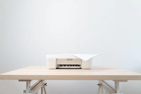 A minimal white printer rests on a light wooden desk with a single sheet of p Stock Photos