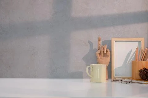 Minimal workplace with empty picture frame, coffee cup and pencil holder on w Stock Photos