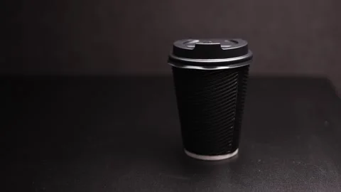 Minimalist black disposable coffee cup with lid on a dark surface, studio Stock Footage 338432553