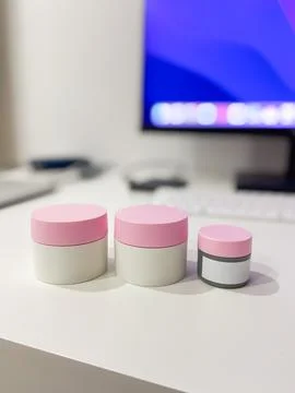 Minimalist desk setup featuring three skincare jars with pink lids, perfect.. Stock Photos