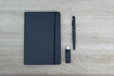 Minimalist flat lay with black notebook, pen and USB flash drive on wood Stock Photos