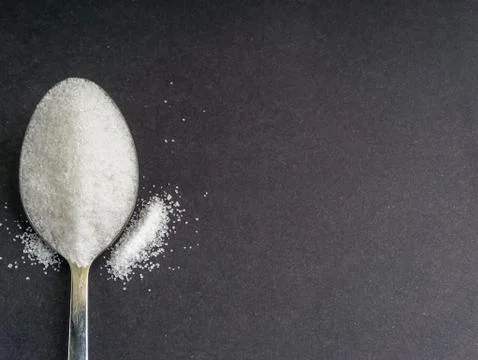Minimalist flat lay composition sugar and spoon on the dark background. 库存照片