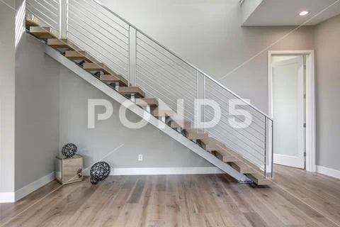 Minimalist foyer boasts stainless steel staircase finished with wood stairs. Stock Photos