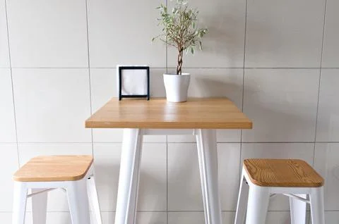 Minimalist high table with two stools, small plant, photo frame, modern setti Stock Photos