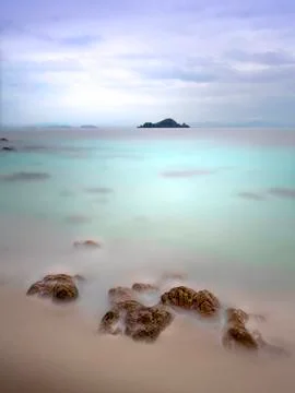 Minimalist long exposure of rock formation in aqua colored calm sea. Stock Photos