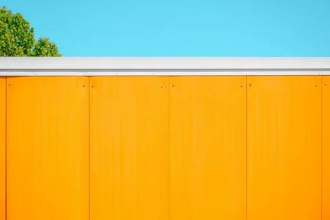 Minimalist orange wall panel facade with blue sky and green tree top overhe.. Stock Photos