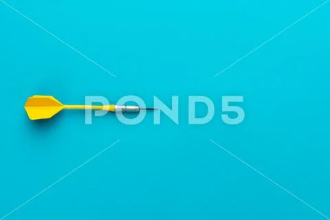 Minimalist photo of yellow plastic dart with metal tip on blue background Stock Photos