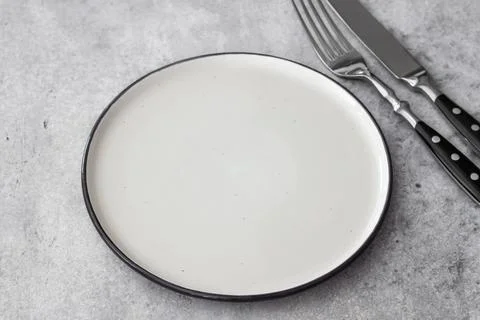 Minimalist top view of an empty white ceramic plate with knife and fork on .. Stock Photos